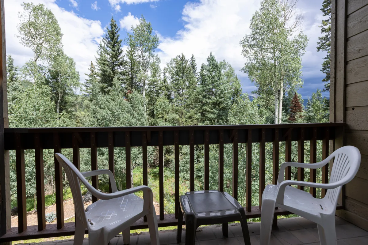 An inviting balcony scene featuring a sturdy railing, two plastic chairs, and a small table. The view opens onto lush greenery, suggesting tranquil surroundings and a direct connection to Durango’s beautiful outdoors. The setup encourages guests to relax, read, or enjoy the sights and sounds of nature.