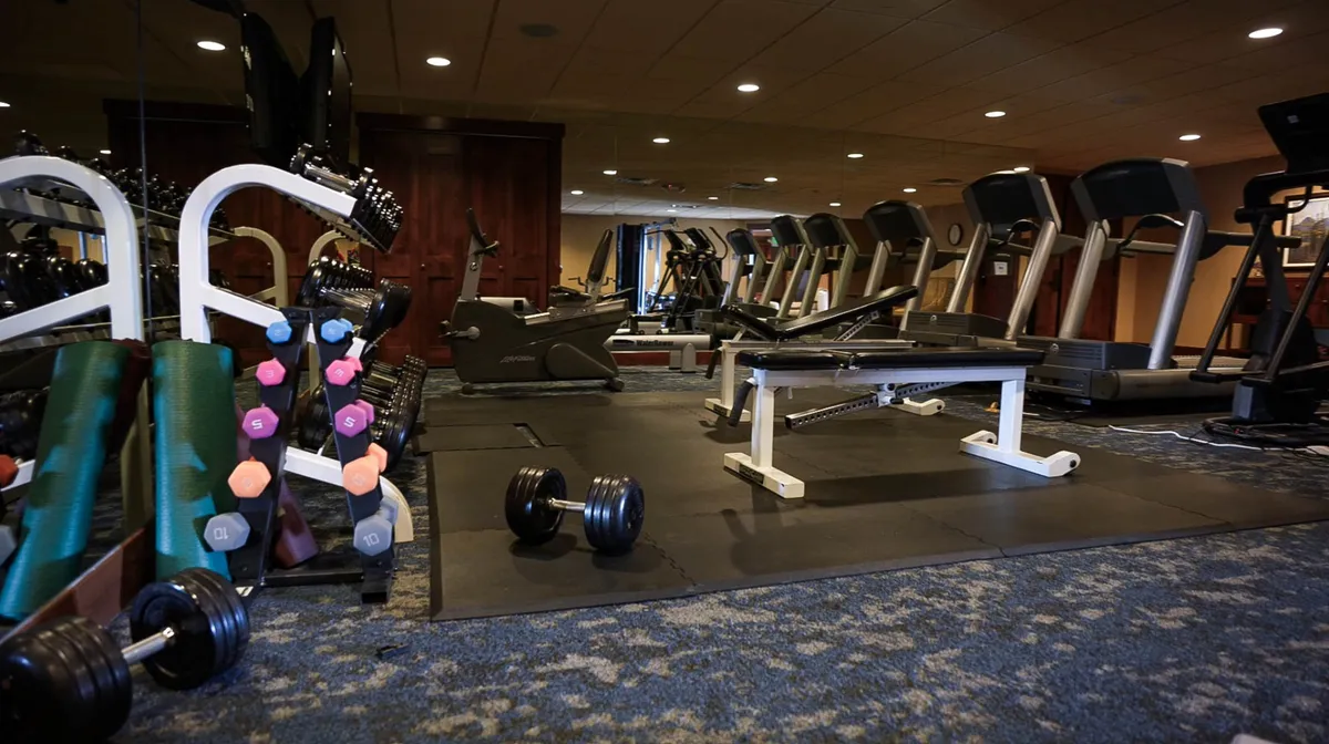 A well-equipped fitness center with dumbbells, treadmills, an exercise bench, and mats. The organized layout and bright lighting create a motivational atmosphere, inviting guests to start active mornings or keep up with their workout routines during their stay.