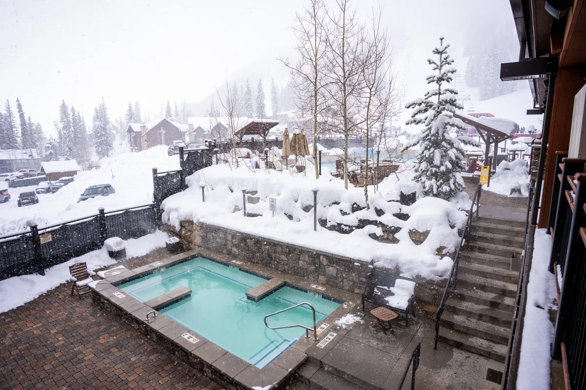The photo captures a steamy outdoor hot tub nestled among snow-covered trees and stepping stones, with a serene, inviting mood. The contrast between the warm water and snowy landscape underscores the sense of relaxation and exclusivity emphasized in the section.