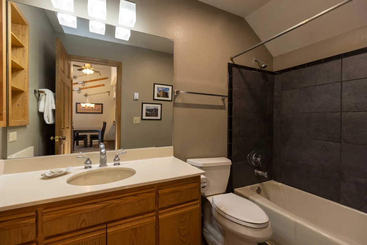 A tranquil bathroom featuring a vanity with sink, a large mirror, a tub and shower combination, and wooden shelving for storage. The ambiance is peaceful and organized, perfect for personal grooming or quiet moments of self-care.