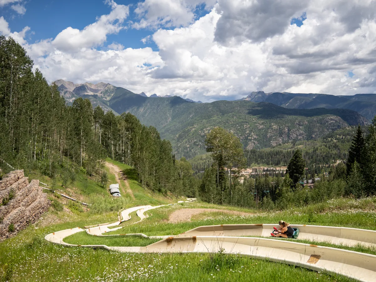 A lively exterior setting with people enjoying a winding slide against a breathtaking mountainous landscape. The image exudes a sense of adventure and joy, highlighting outdoor leisure activities suitable for families and children.