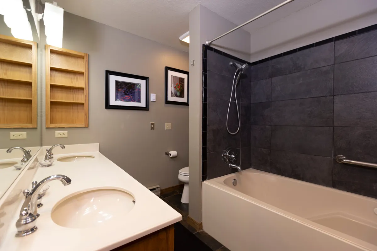 A modern bathroom with double vanity sinks, elegant framed artwork, and a spacious bathtub. The space is bright and serene, inviting relaxation and comfort for morning or evening routines.