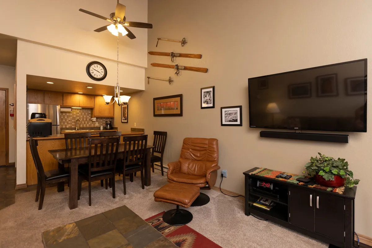 A welcoming view of the dining area and kitchen, featuring a family-sized table, a modern kitchen area in the background, a cozy leather chair, and decorative touches like wall art. The scene feels both functional and inviting, reinforcing the social and culinary elements.