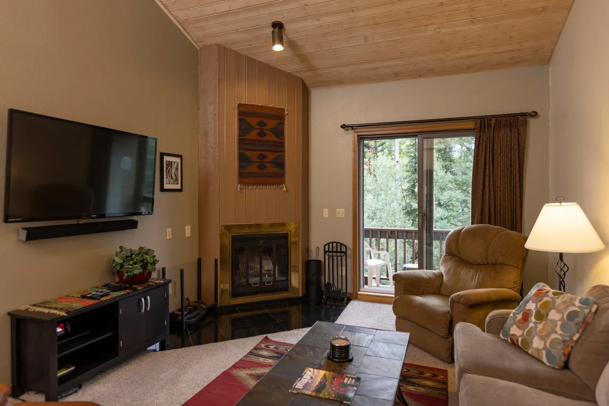 A cozy, spacious interior lounge area featuring a large window overlooking the outdoors, a warm fireplace, a comfortable seating area, and a TV—perfect for family gatherings, post-activity relaxation, or social time.