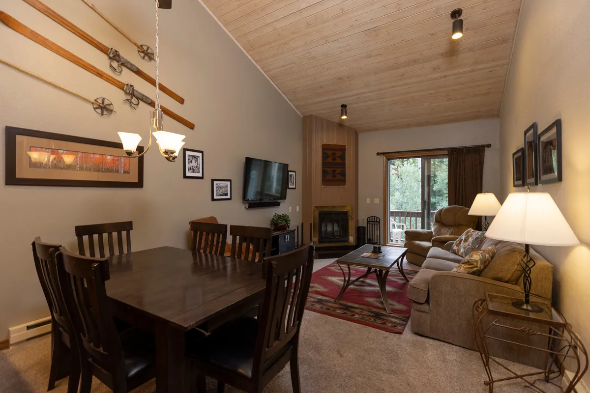 This image showcases a spacious open-concept area with a family-sized dining table, a cozy sofa, a warm fireplace, and a television. The layout encourages gatherings and socializing, with seamless flow between the living and dining spaces.